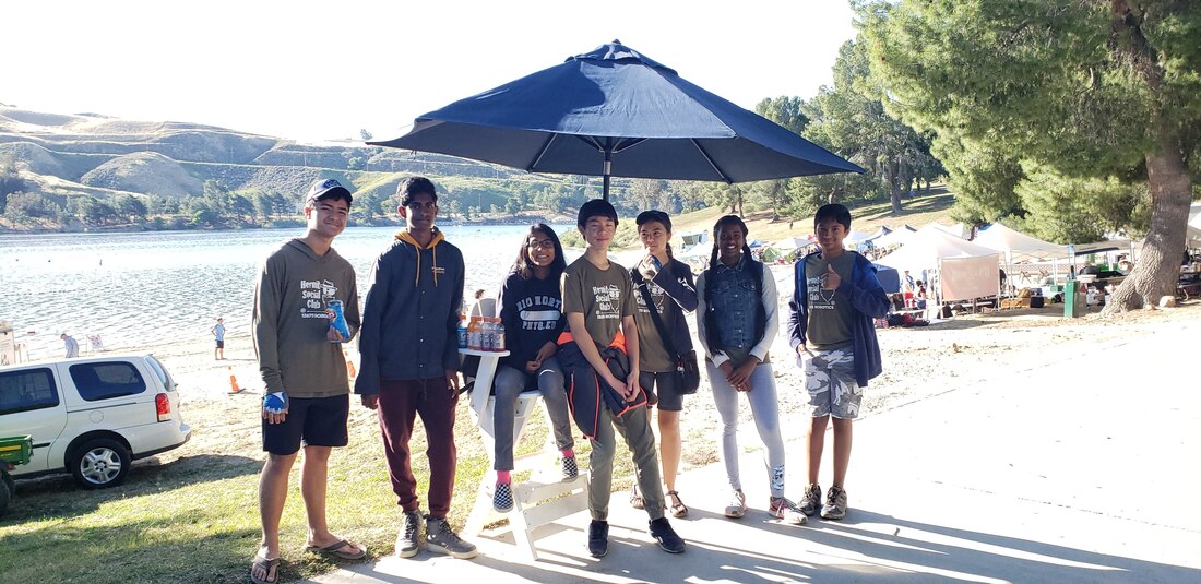 team members stand around a chair with an umbrella, in the background is Castaic Lake